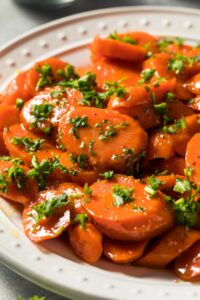 Sliced glazed carrots on plate garnished with chopped parsley leaves.