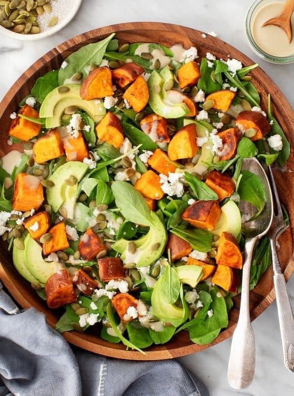 Sweet potato salad in wooden bowl with roasted sweet potato, feta, avocado, and leafy spinach. 