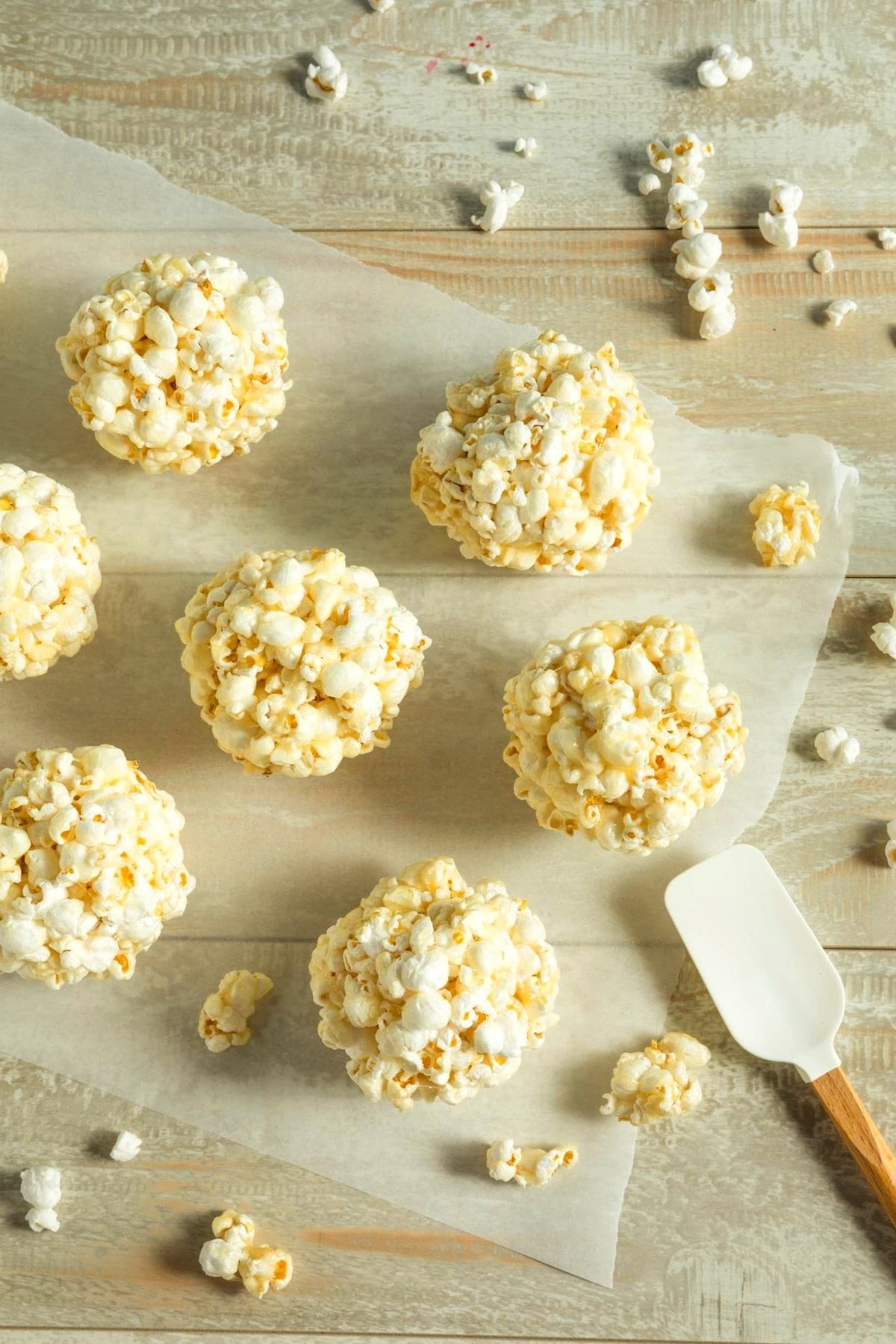 Popcorn balls laid on a parchment paper on top of a wooden table.