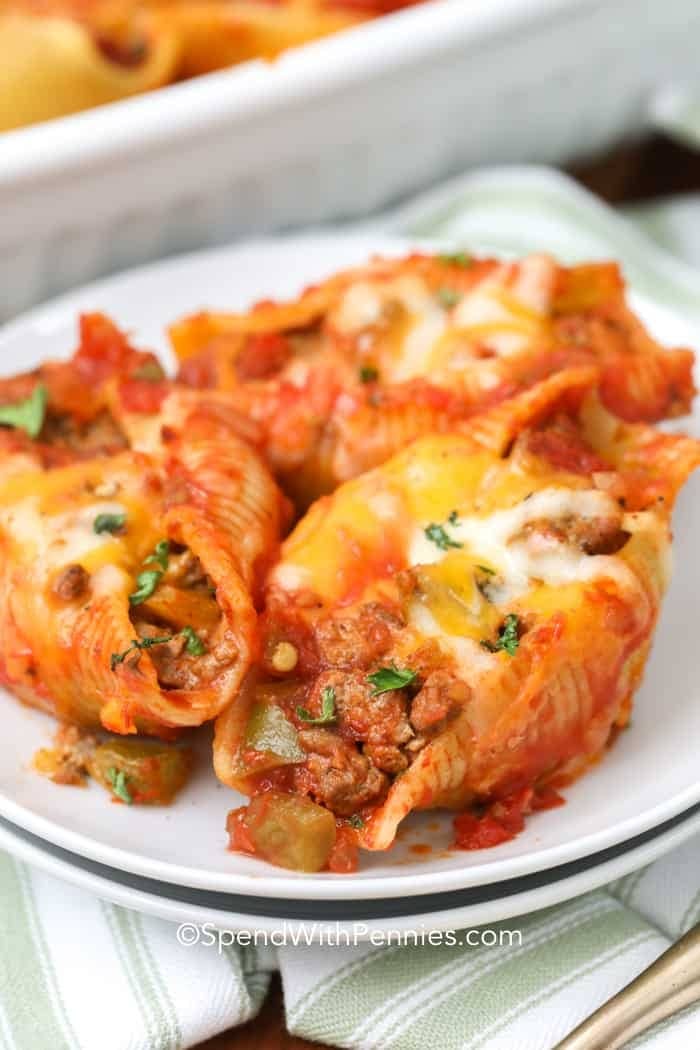 A serving of taco stuffed shells on a plate topped with melted cheese and cream garnished with chopped herbs. 