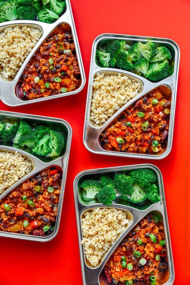 Tempeh chili meal prep made with tempeh, beans, and spices served with rice and green vegetables. 