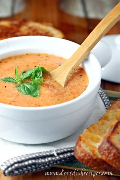 Wooden spoon dipped in a bowl of Tomato Parmesan Soup garnished with basil leaves