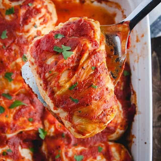 A spoon lifting a slice of turkey stuffed cabbage rolls from a casserole dish. 