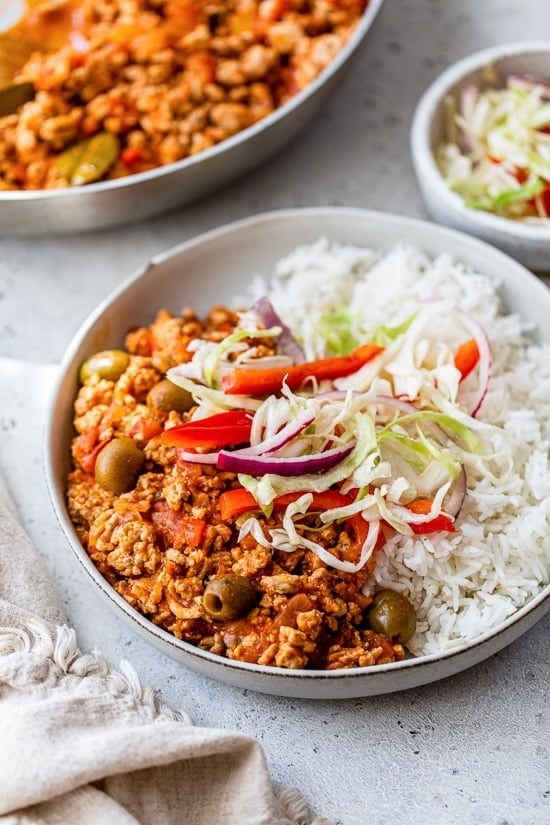 Turkey picadillo served on a bowl of white rice garnished with fresh veggies and onions. 