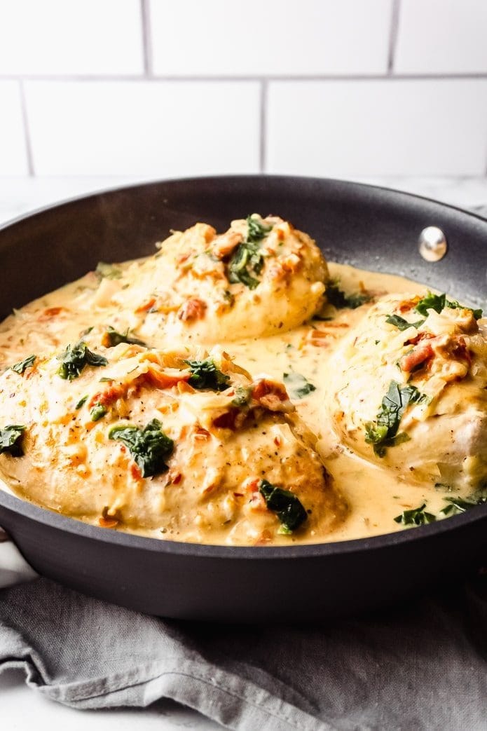 Tuscan chicken cooked in pan with white creamy sauce and chopped parsley leaves. 