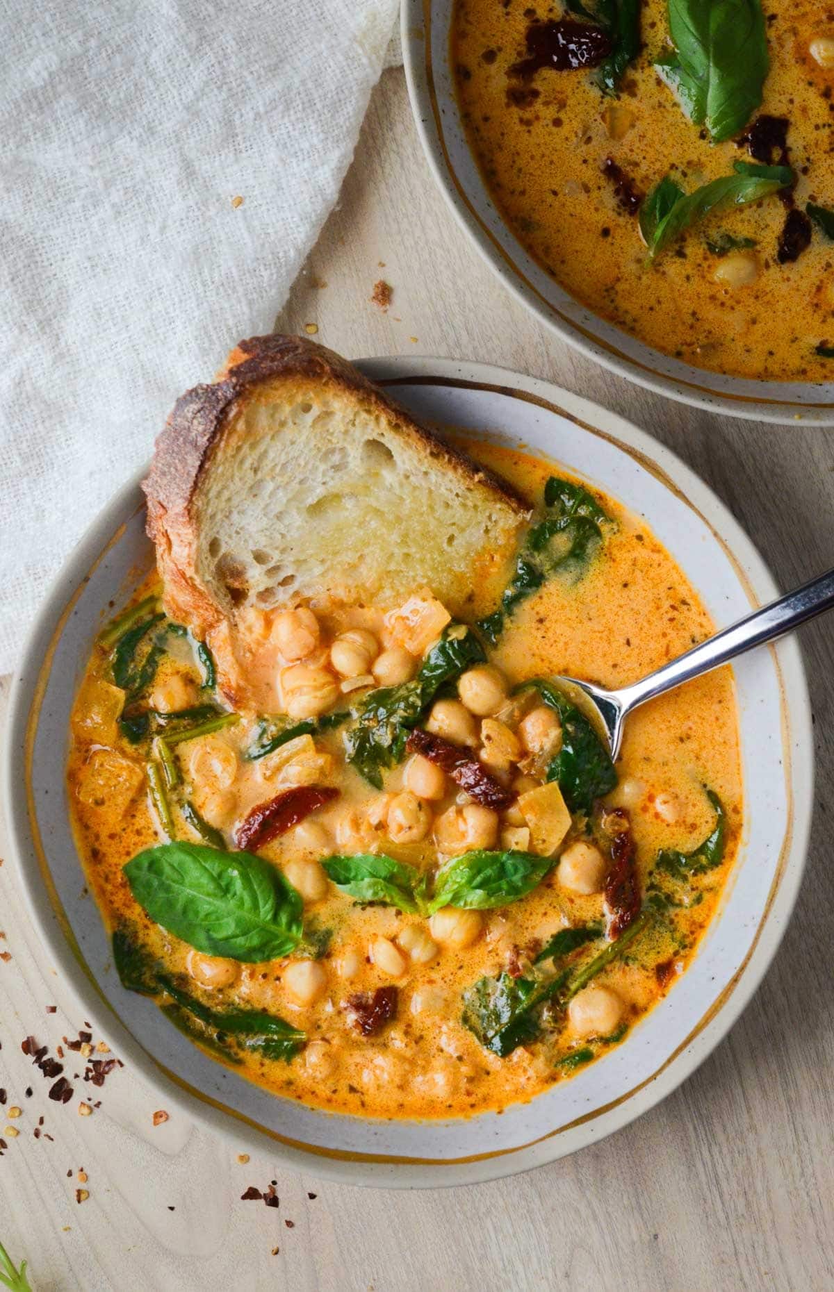 Sliced bread dipped on a bowl of homemade Vegan Tuscan Chickpea Soup