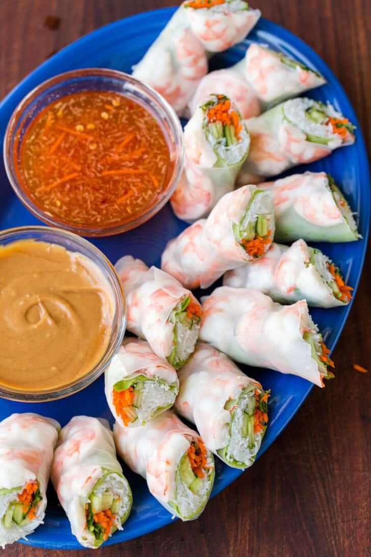Cut in half fresh spring rolls in blue plate served with dipping sauces. 
