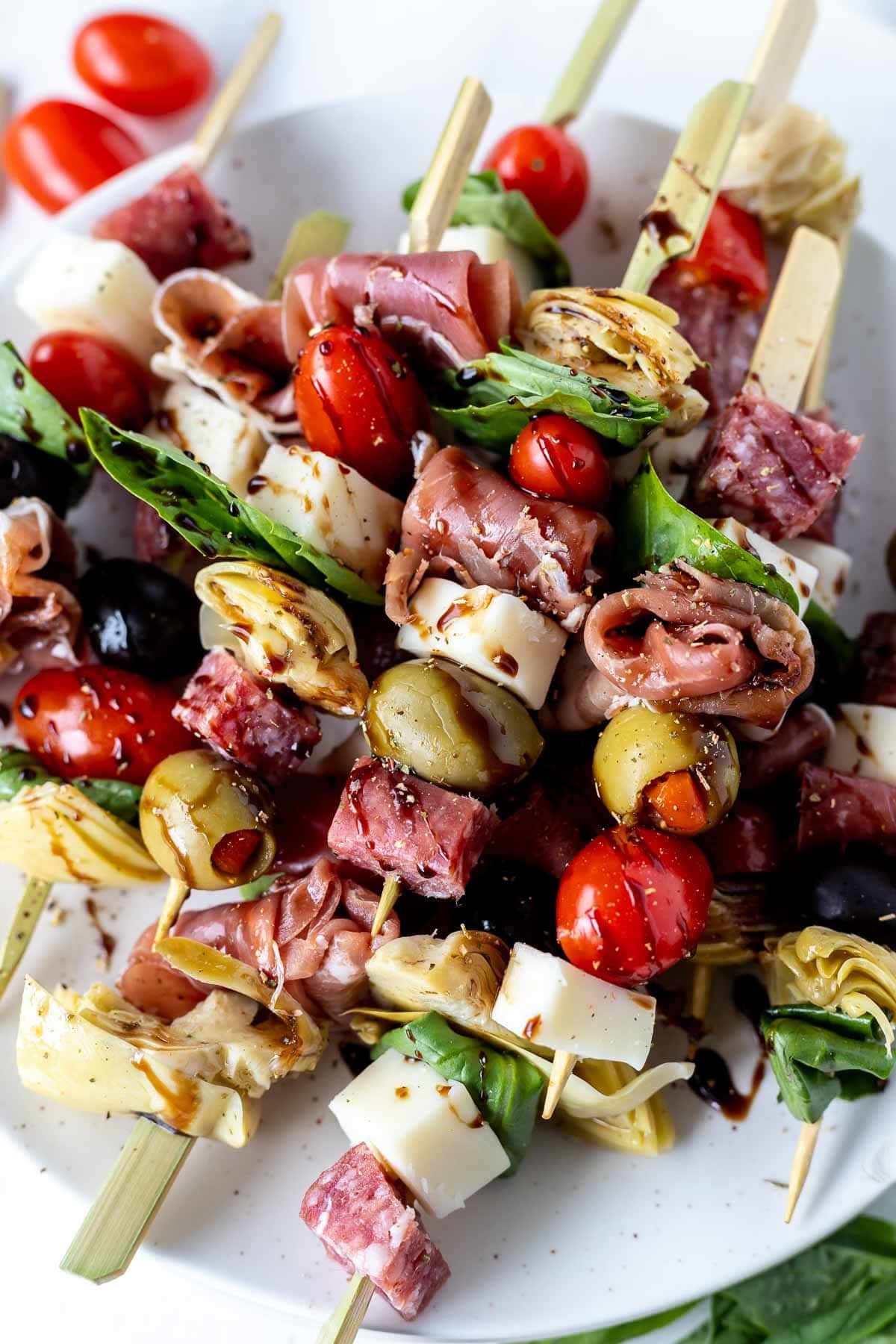 Antipasto skewers made with meat, cheese, olives and cherry tomatoes drizzled with sauce. 