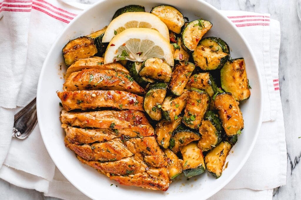 Asado chicken breast with sauteed lemon zucchini served on a white plate. 