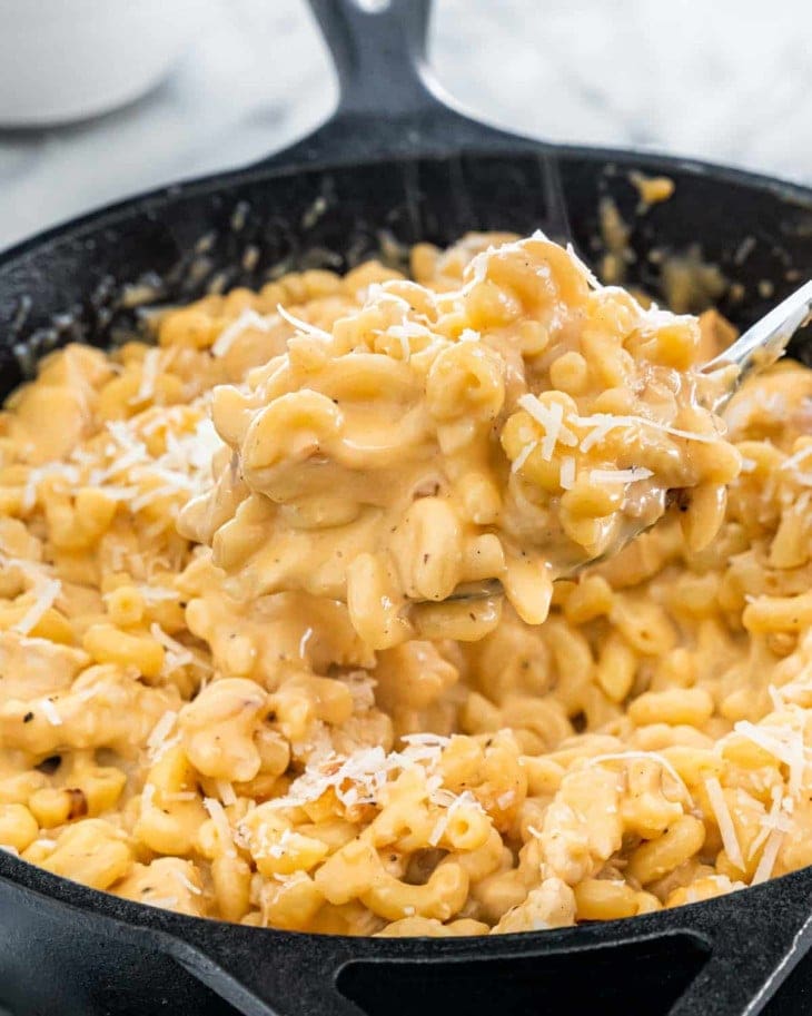 Cheese chicken mac and cheese cooked on a stoneware scooped with a ladle. 