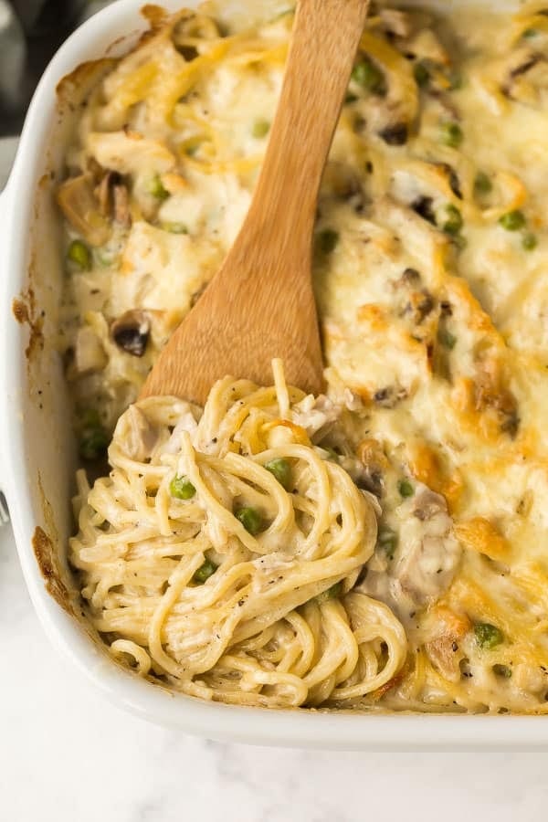 Chicken Tetrazzini made with past, veggies and cheese on a white dish mixed with a wooden spoon. 