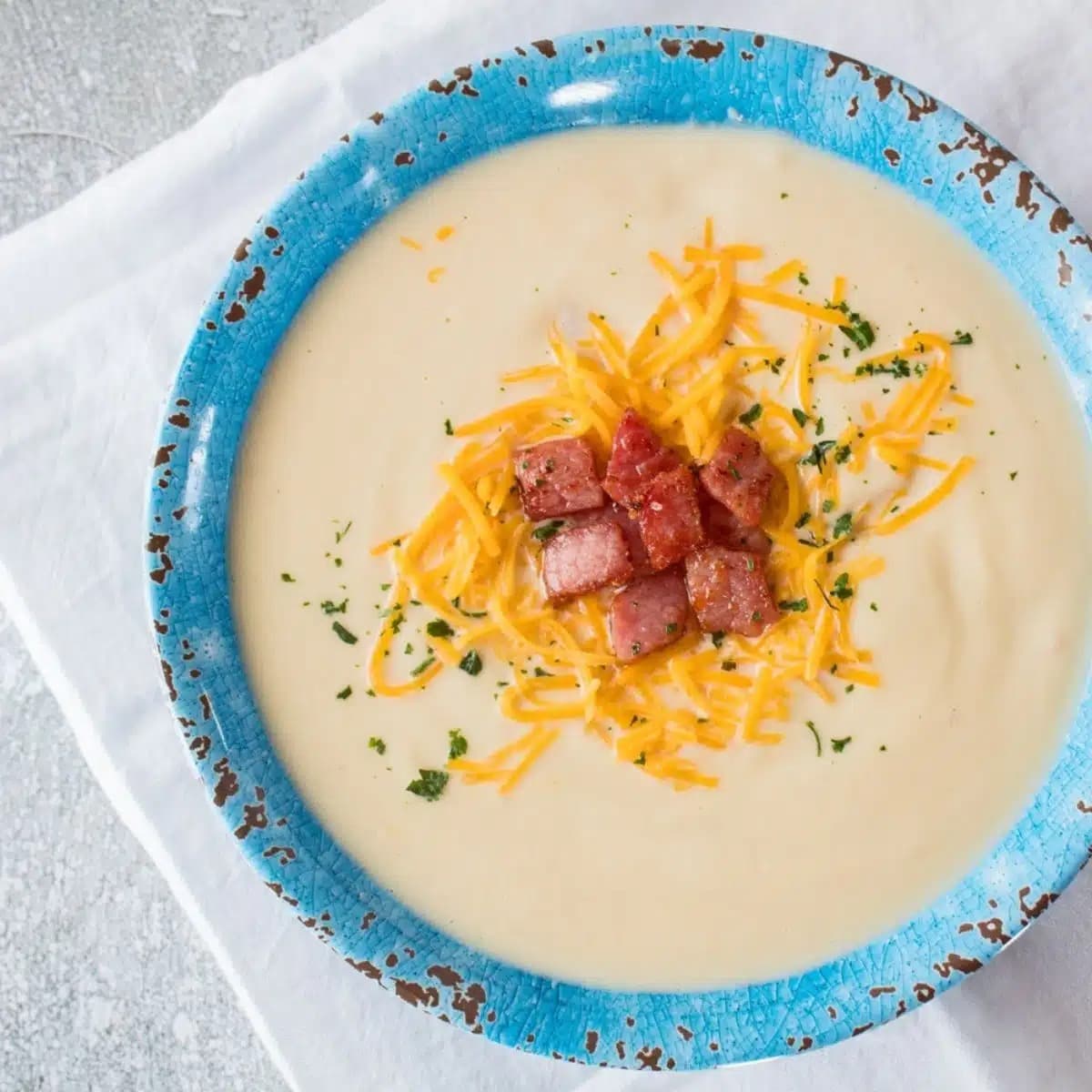 Creamy cauliflower ham soup served on a bowl topped with grated cheese and cooked ham. 