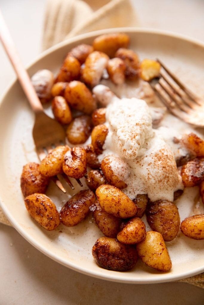 Gnocchi with sugar, cinnamon and and creamy coconut whip served on a plate with fork. 