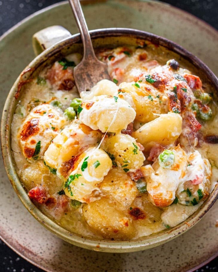 Bowl of ham and cheese gnocchi with bacon and peas. 