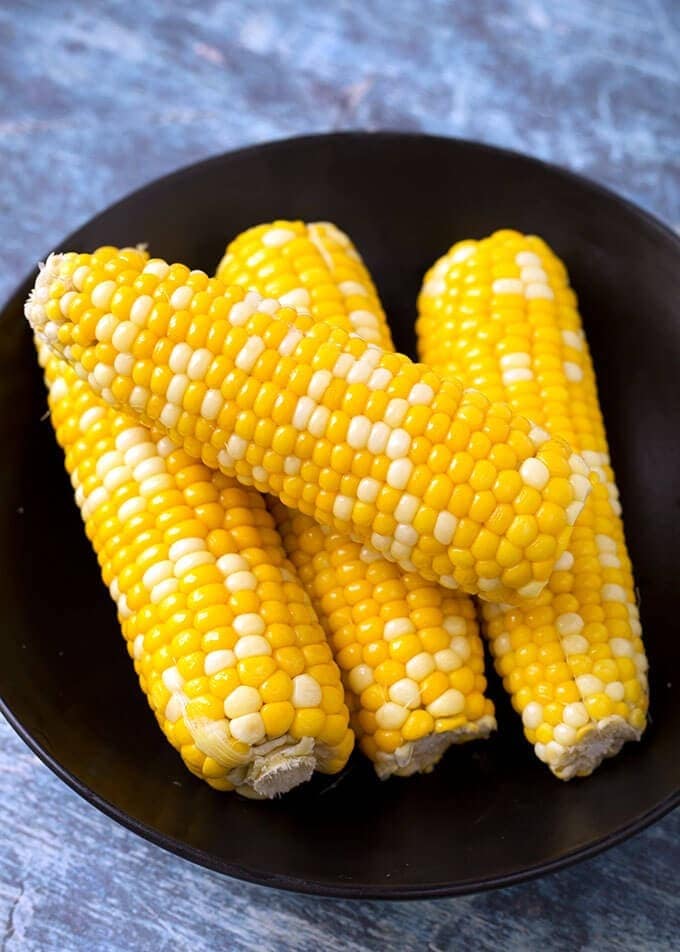 Black plate with cooked corn on the cob. 