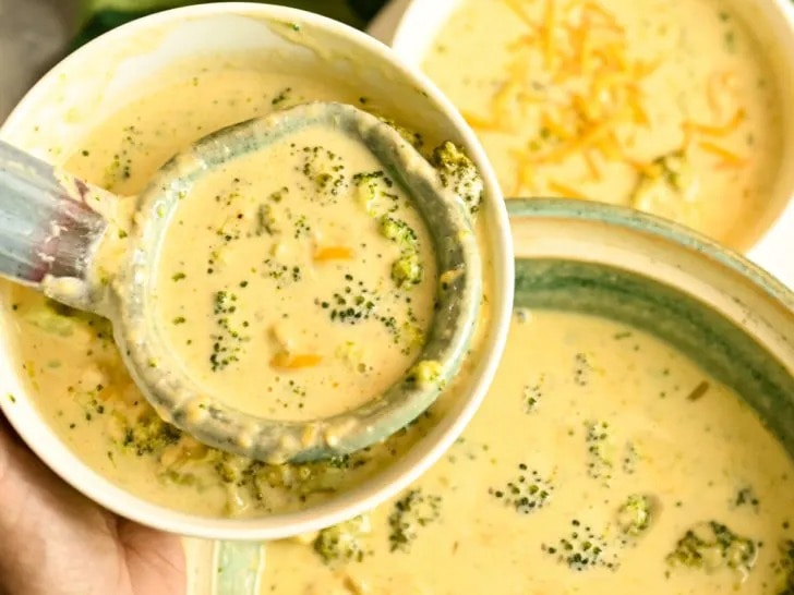 Broccoli cheddar soup in pot and bowl scooped with ladle. 