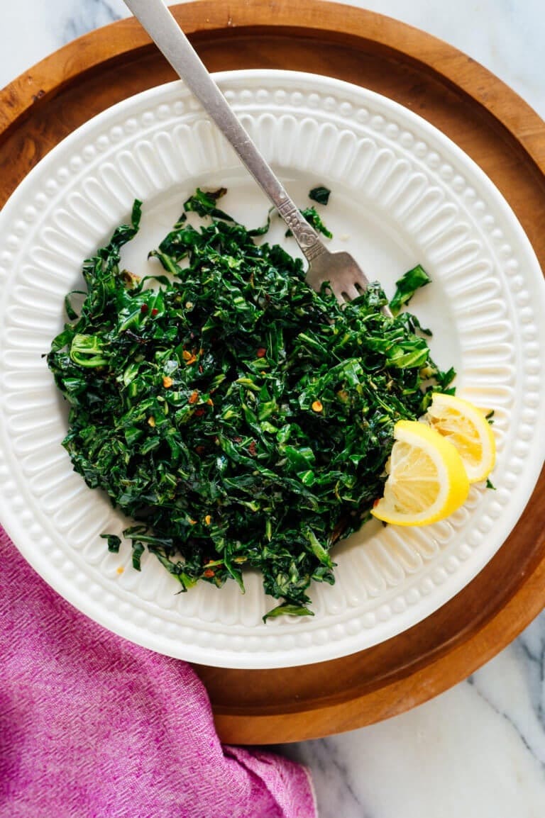 Collard greens with sliced lemon on sides served on a white plate with fork. 
