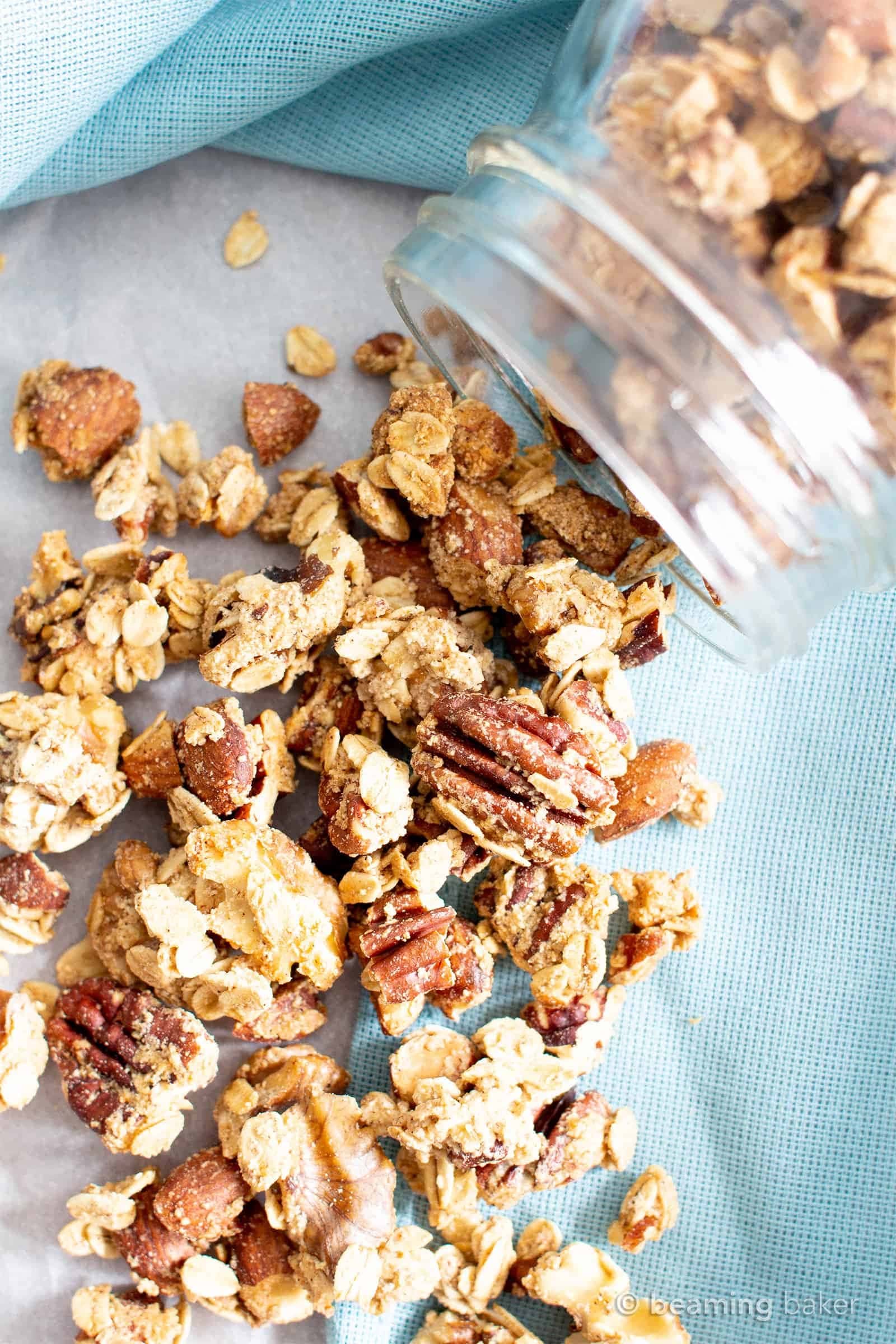 Clusters of crunchy granola poured from a glass jar.