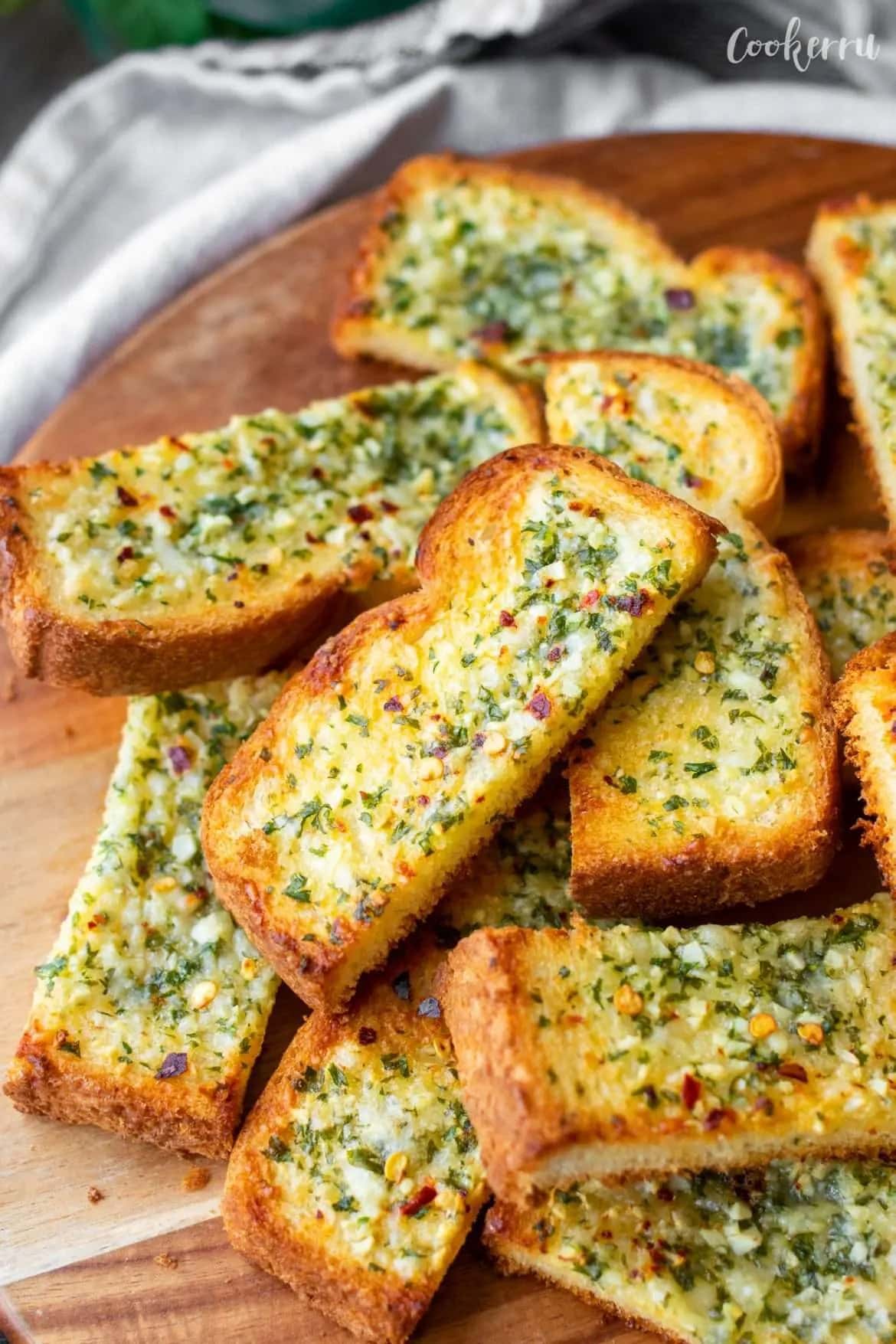Baked slices of bread  on a wooden board with butter garlic spread on top.