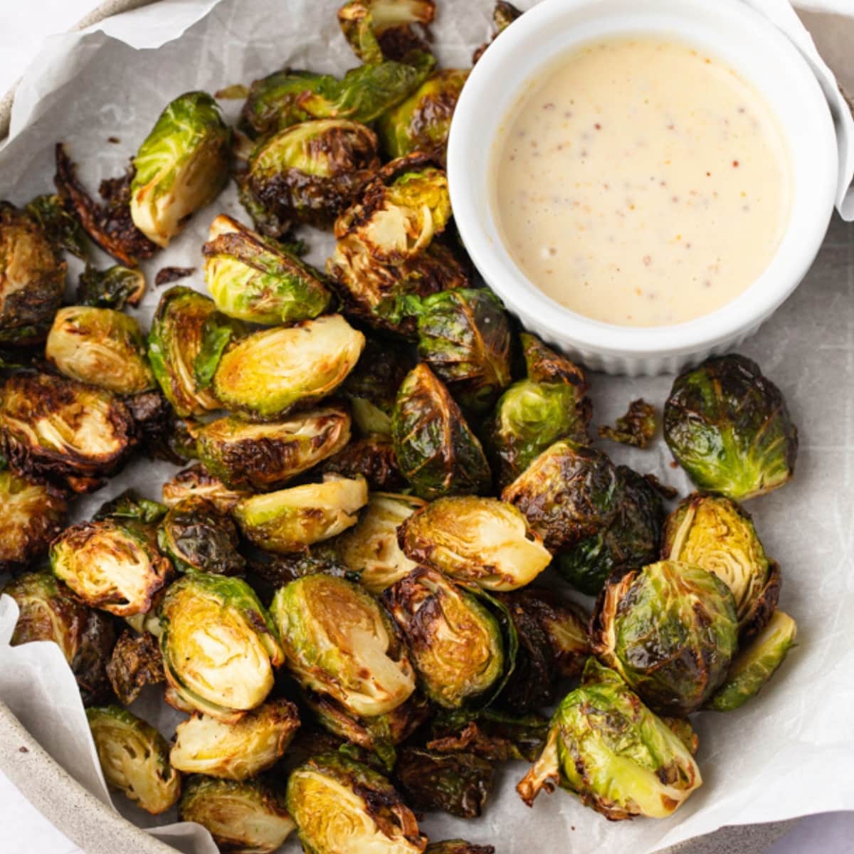 Bunch of roasted brussels sprouts on a plate with dipping sauce.