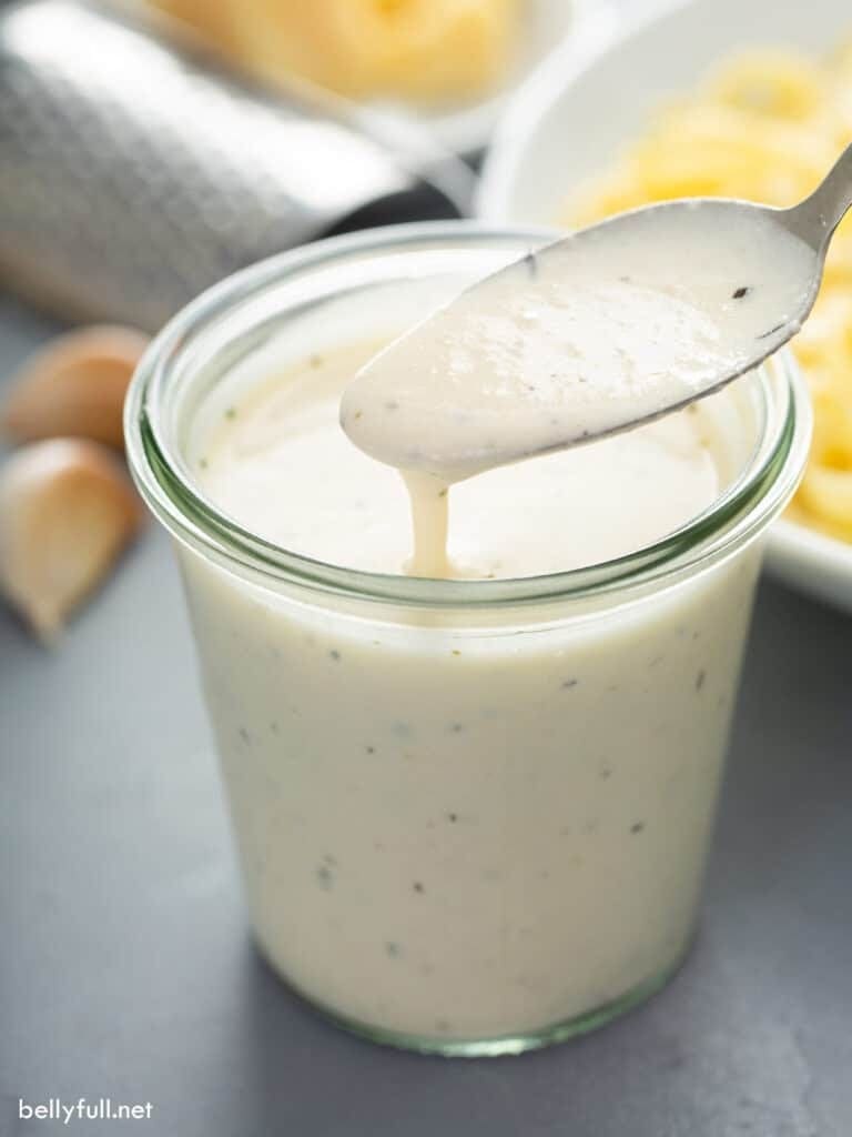 Spoon dripping with alfredo sauce on a glass jar. 