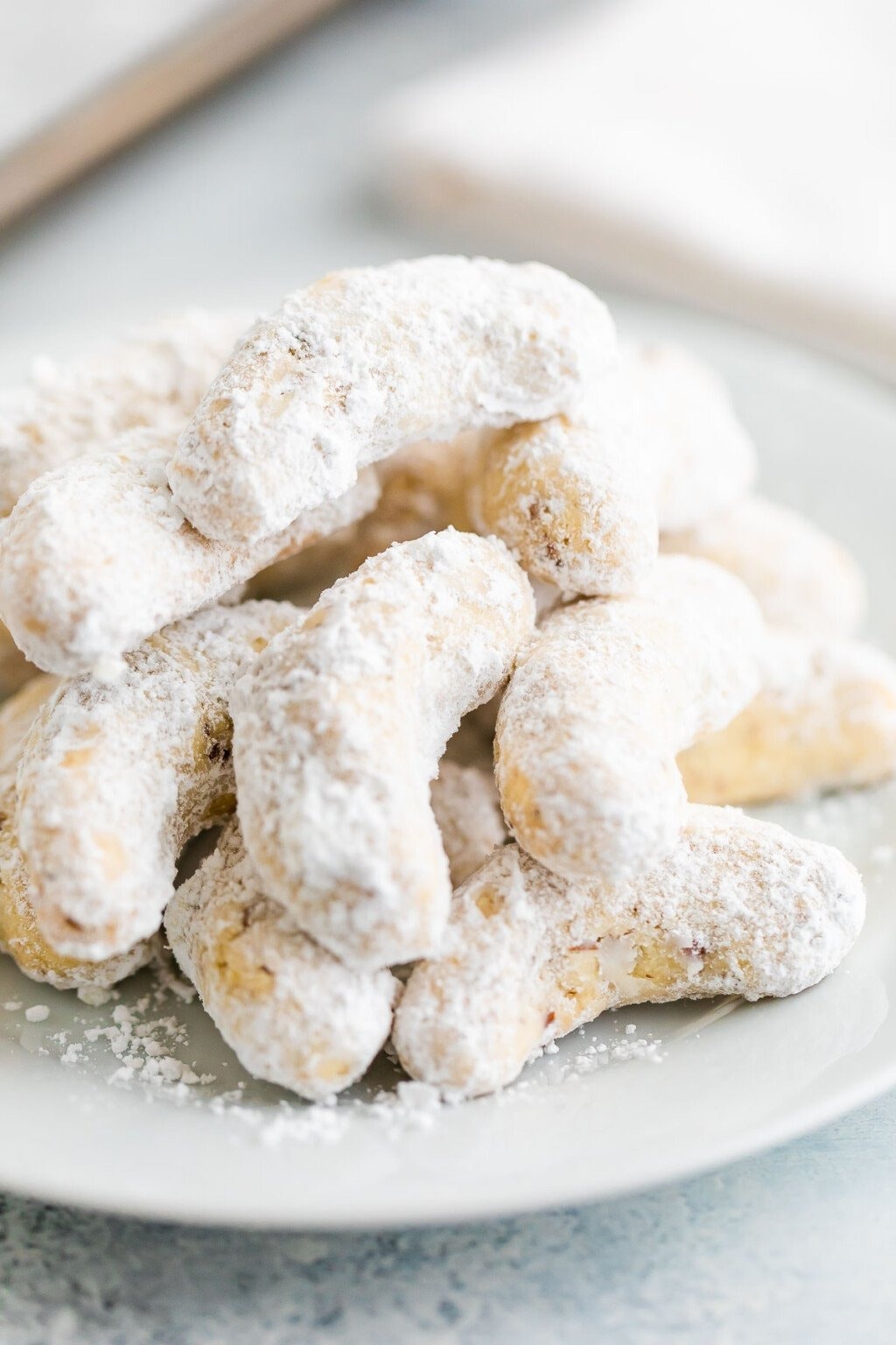 Bunch of crescent shaped cookies covered with powdered sugar on a plate. 