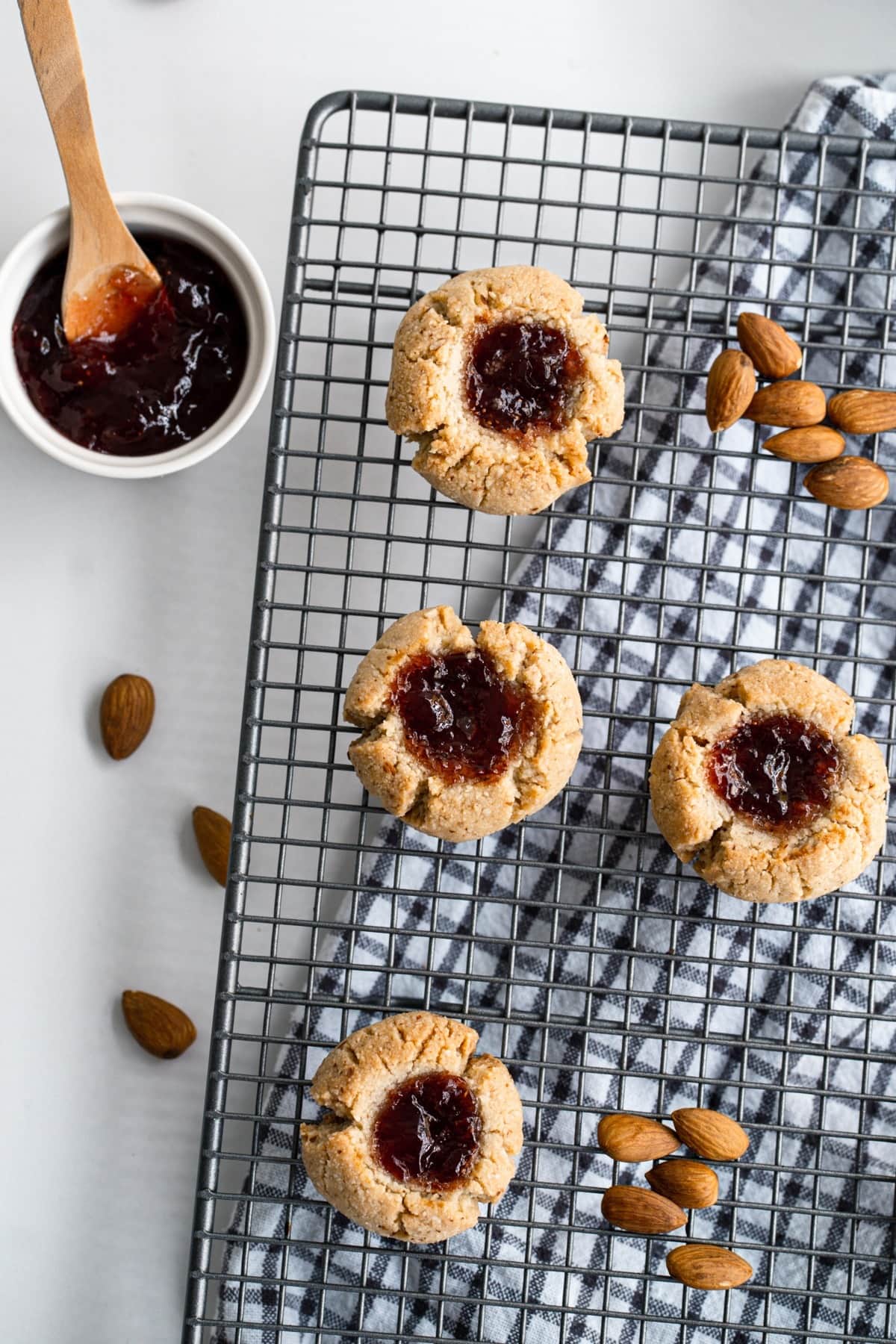 Thumbprint cookies with jam filling and pieces of almonds on a cooling rack.