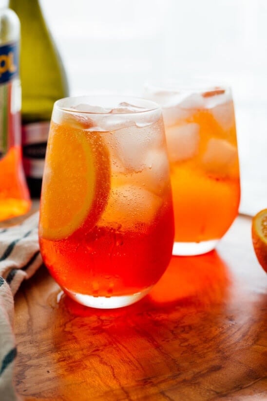 Two glasses of refreshing Aperol spritz, an Italian cocktail, placed on a rustic wooden cutting board.