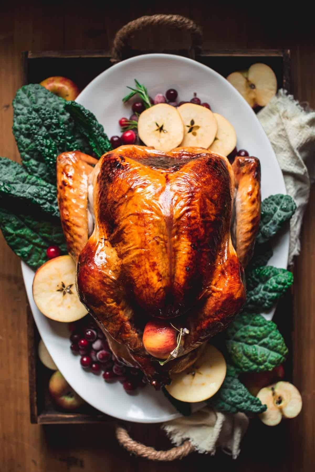 Roasted whole turkey served with apple slices, cranberries and a bed of green leaves.  