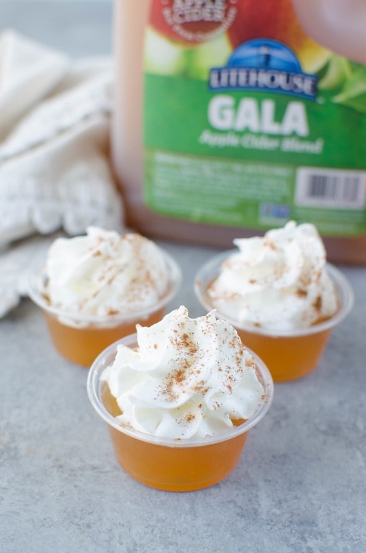 Apple cider Jello shots on plastic cup topped with a dollop of whipped cream.