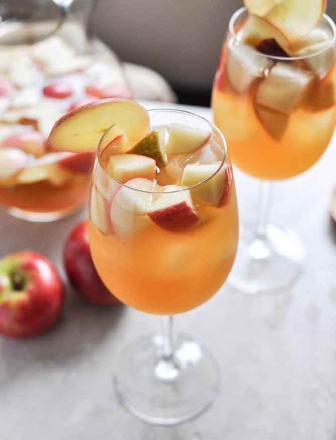 Apple cider sangria on wine glasses garnished with floating chopped apples. 