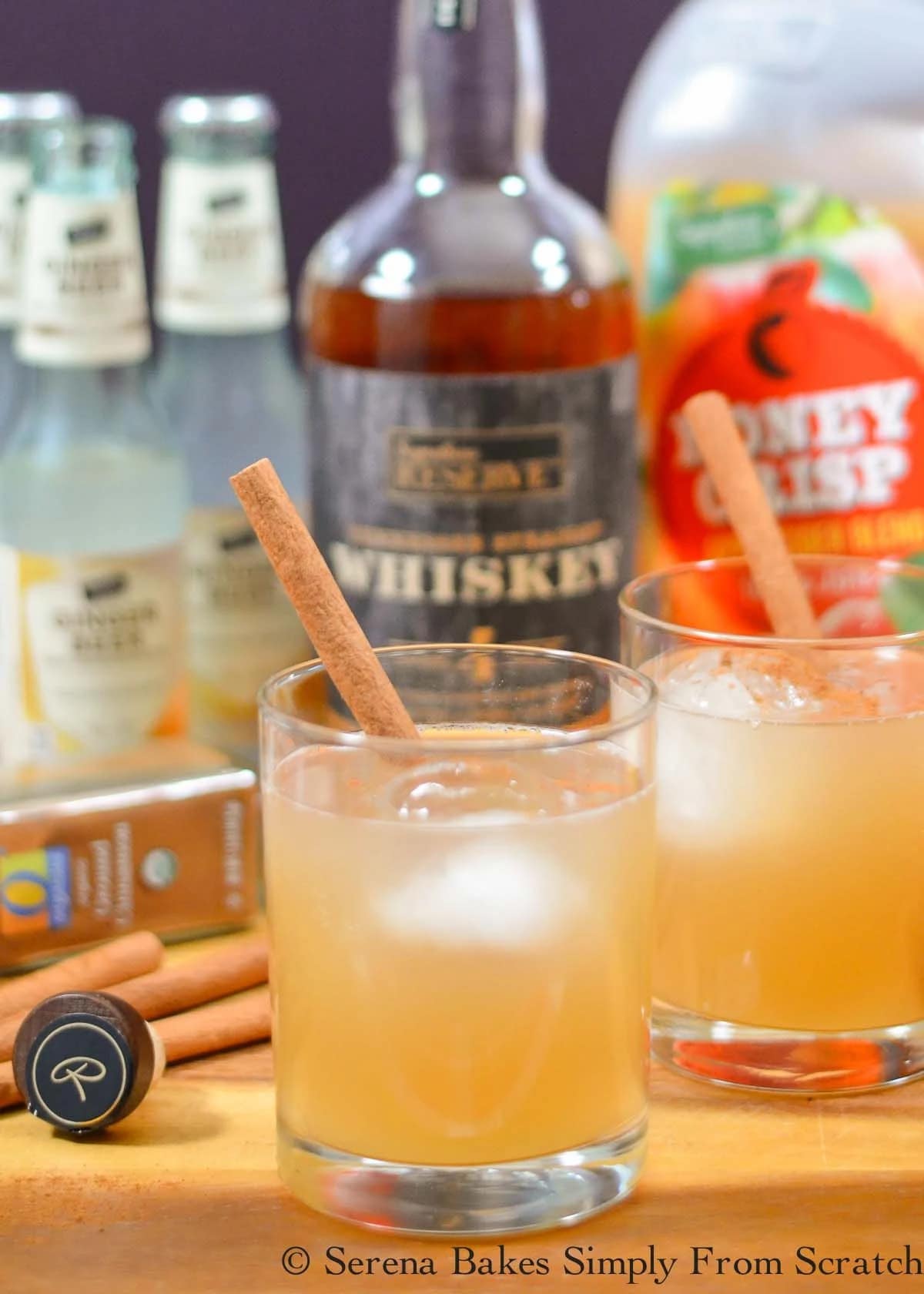 Boozy homemade apple cider whiskey and ginger beer in two glasses with cinnamon stick garnish