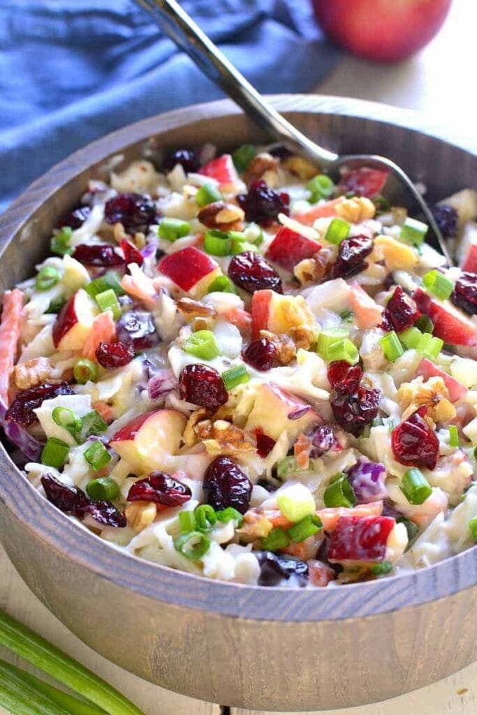 Coleslaw in a wooden bowl made with chopped apples, walnuts, and dried cranberries. 