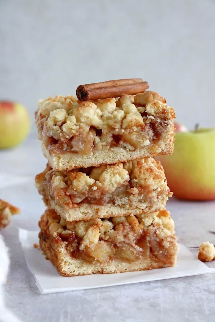 Stack of apple crumble bars topped with cinnamon stick. 
