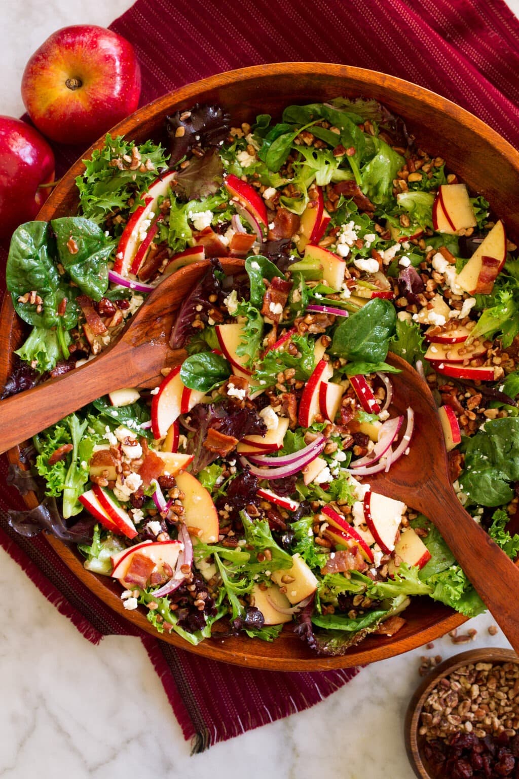 Wooden bowl with salad toss of spinach, feta, apple, pecans, and red onion into a bowl. 