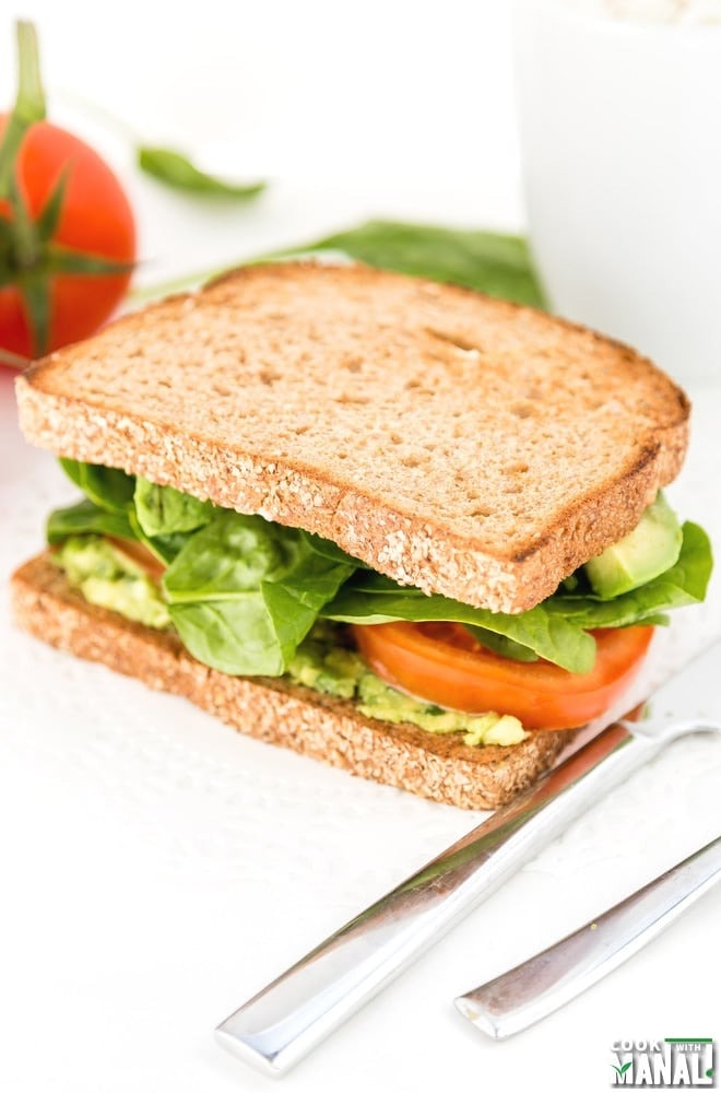 Wheat bread sandwich with sliced tomato, arugula and avocado dressing. 