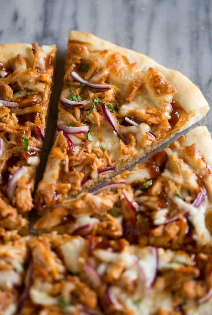 Sliced pizza with shredded chicken meat, red onion and sauce toppings.