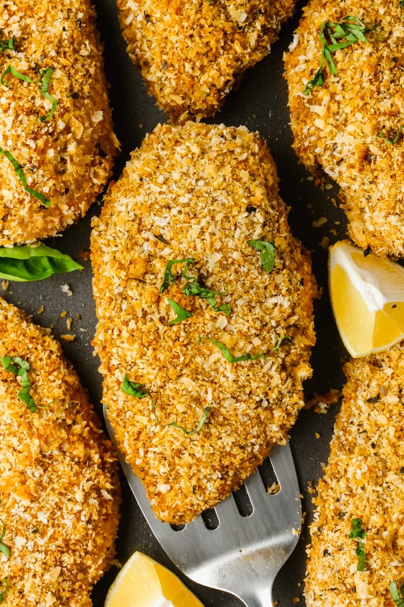 Chicken coated in bread crumbs and parmesan cheese on a pan. 