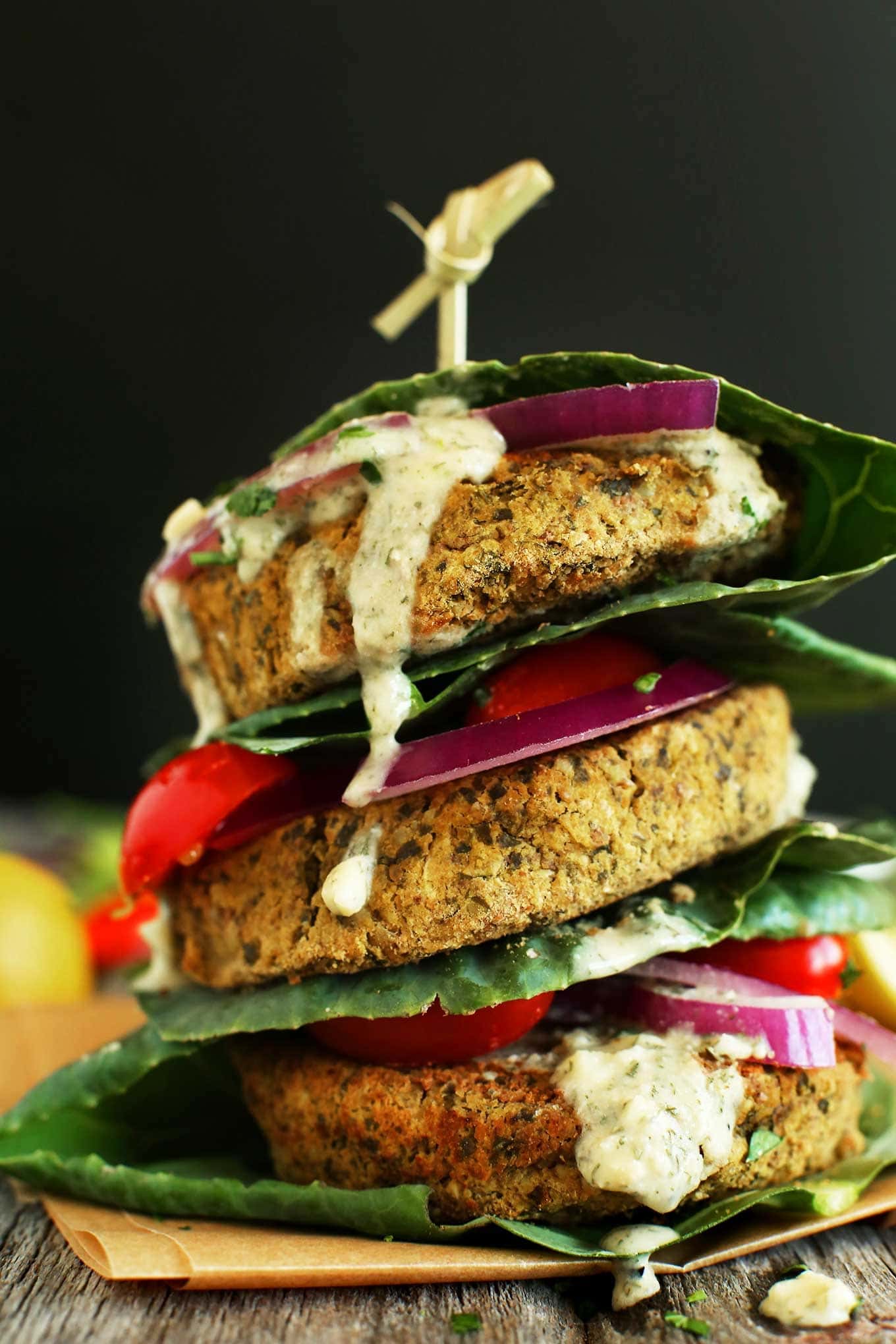 Falafel burgers with lettuce, tomatoes, onions stacked on top of each other with mayo dressing dripping on the side