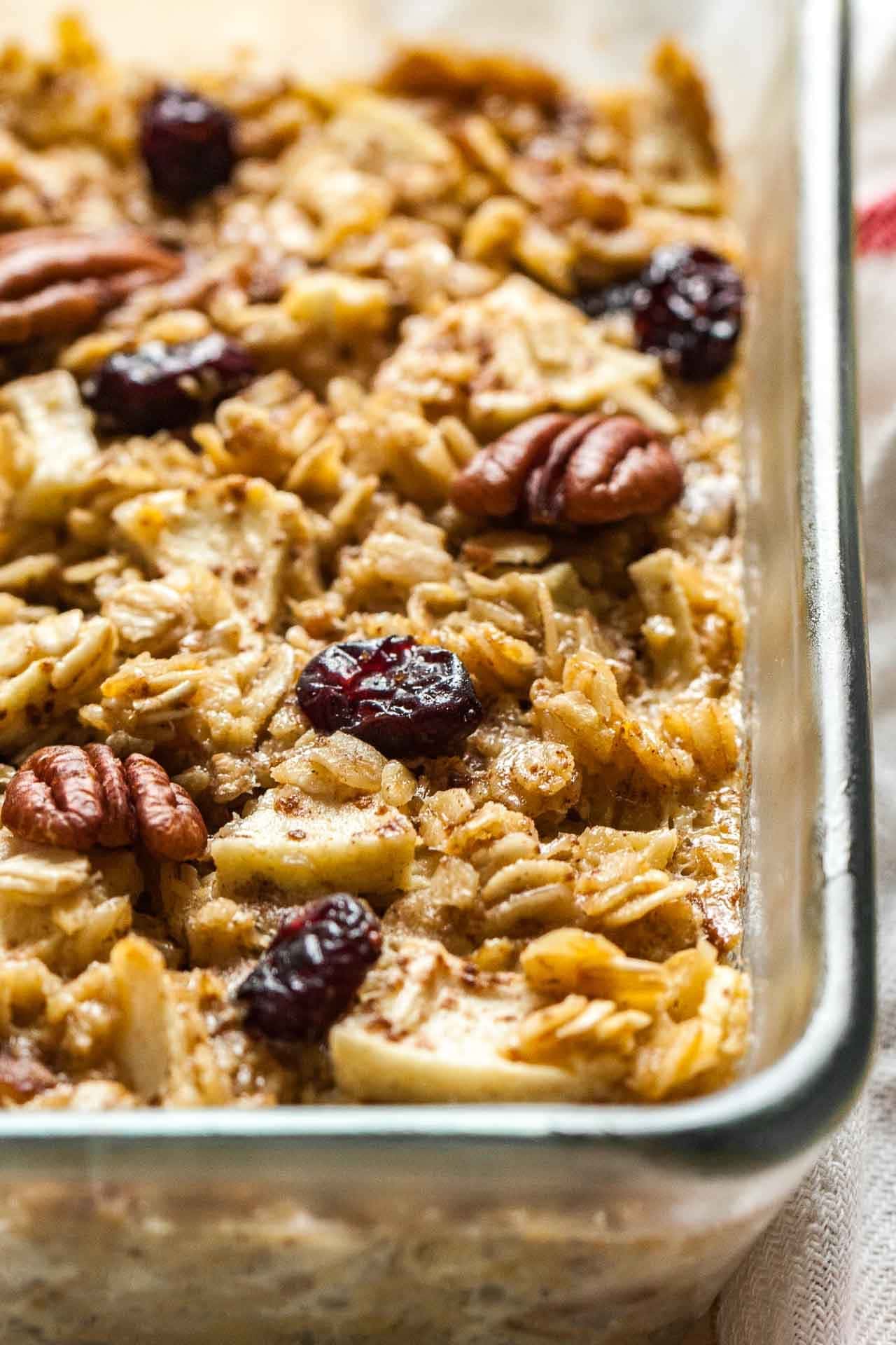 Baked oatmeal with apples, pecans, and cranberries on a glass baking dish.