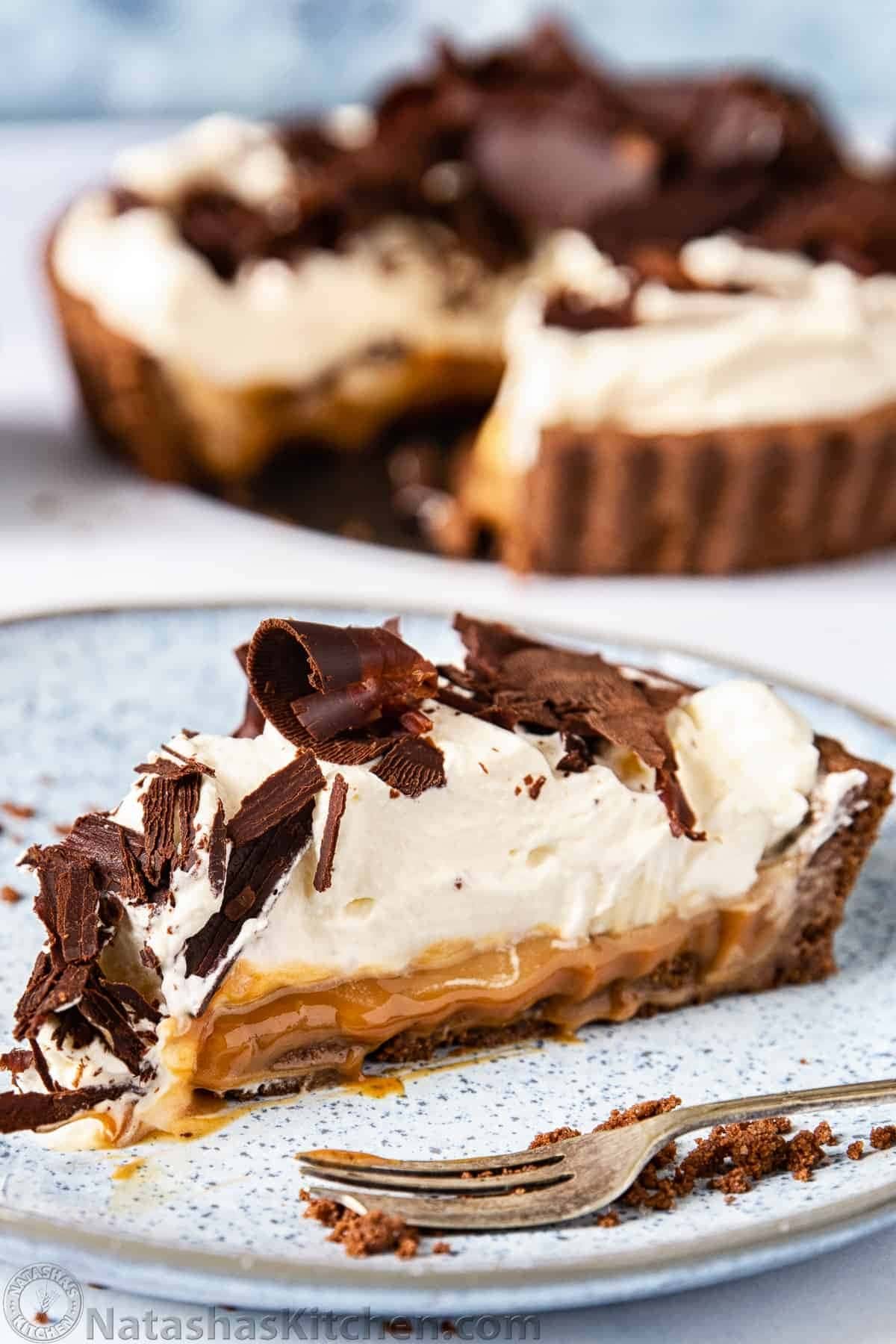 A slice of banoffee pie with layers of caramel, whipped cream and chocolate shavings on top.