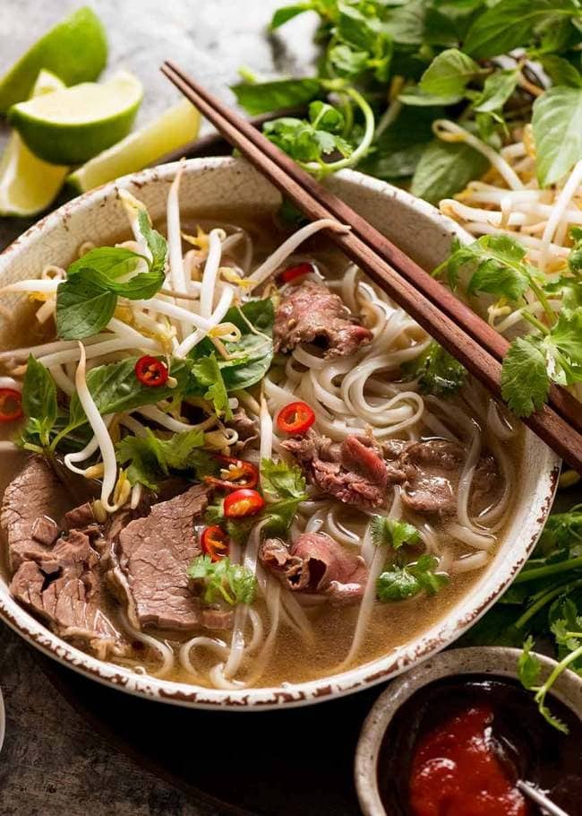 A bowl of pho with beef slices, bean sprouts, chopped chili and parsley leaves. 