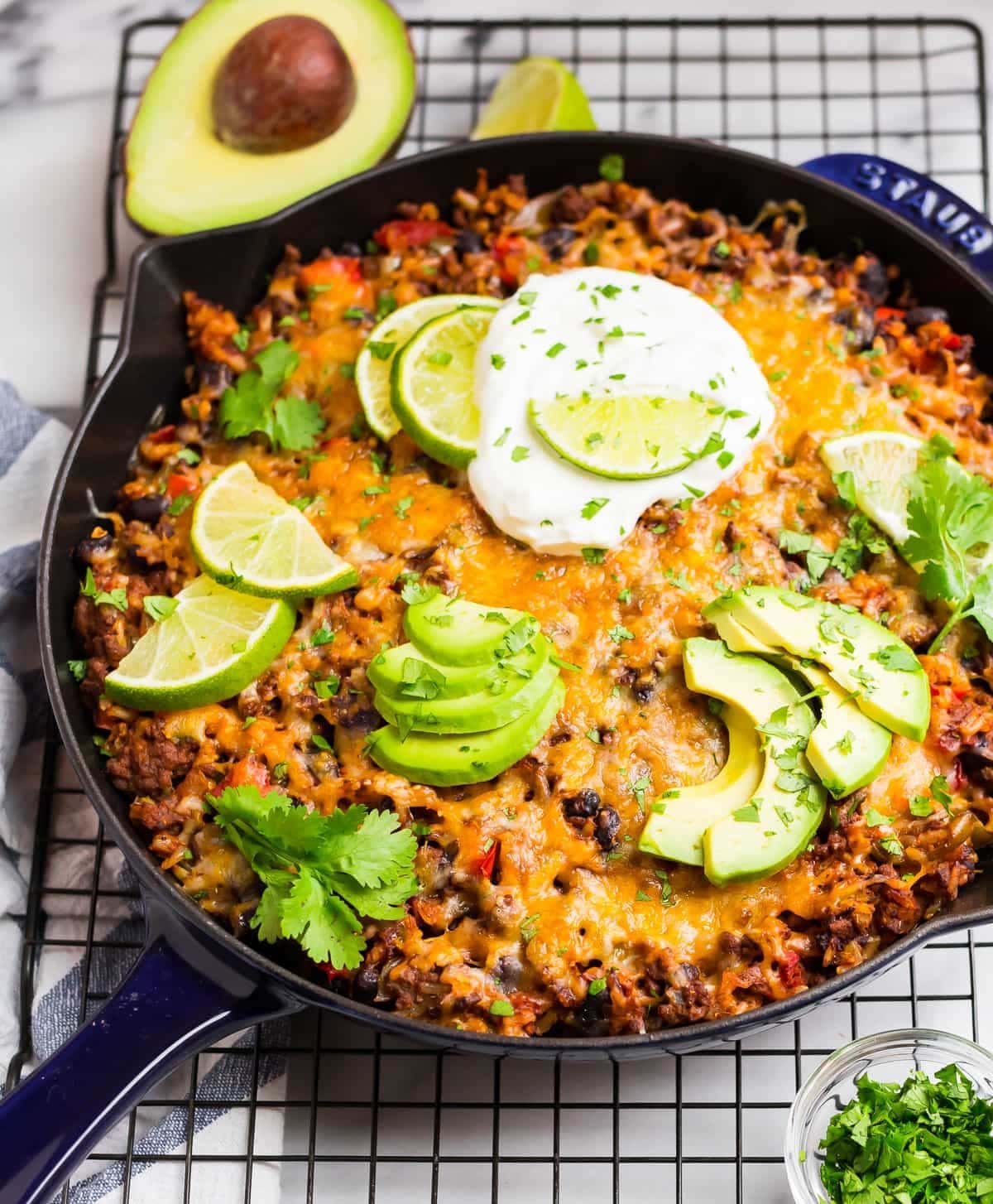Cast iron pan with lean, ground beef, rice, black beans, cheese and garnished with slice lime, avocados and chopped parsley