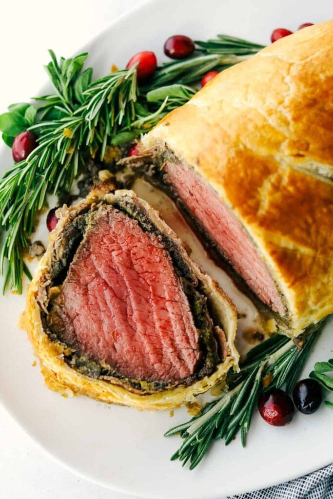 Beef tenderloin with a layer of mustard, mushroom duxelles, and prosciutto wrapped in a soft, buttery pastry sliced, served on a platre. 