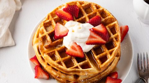 Stack of Belgian Waffles with sliced strawberries and whipped cream on top