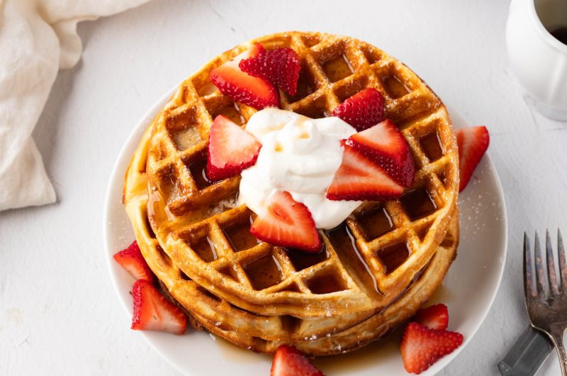 Stack of Belgian Waffles with sliced strawberries and whipped cream on top