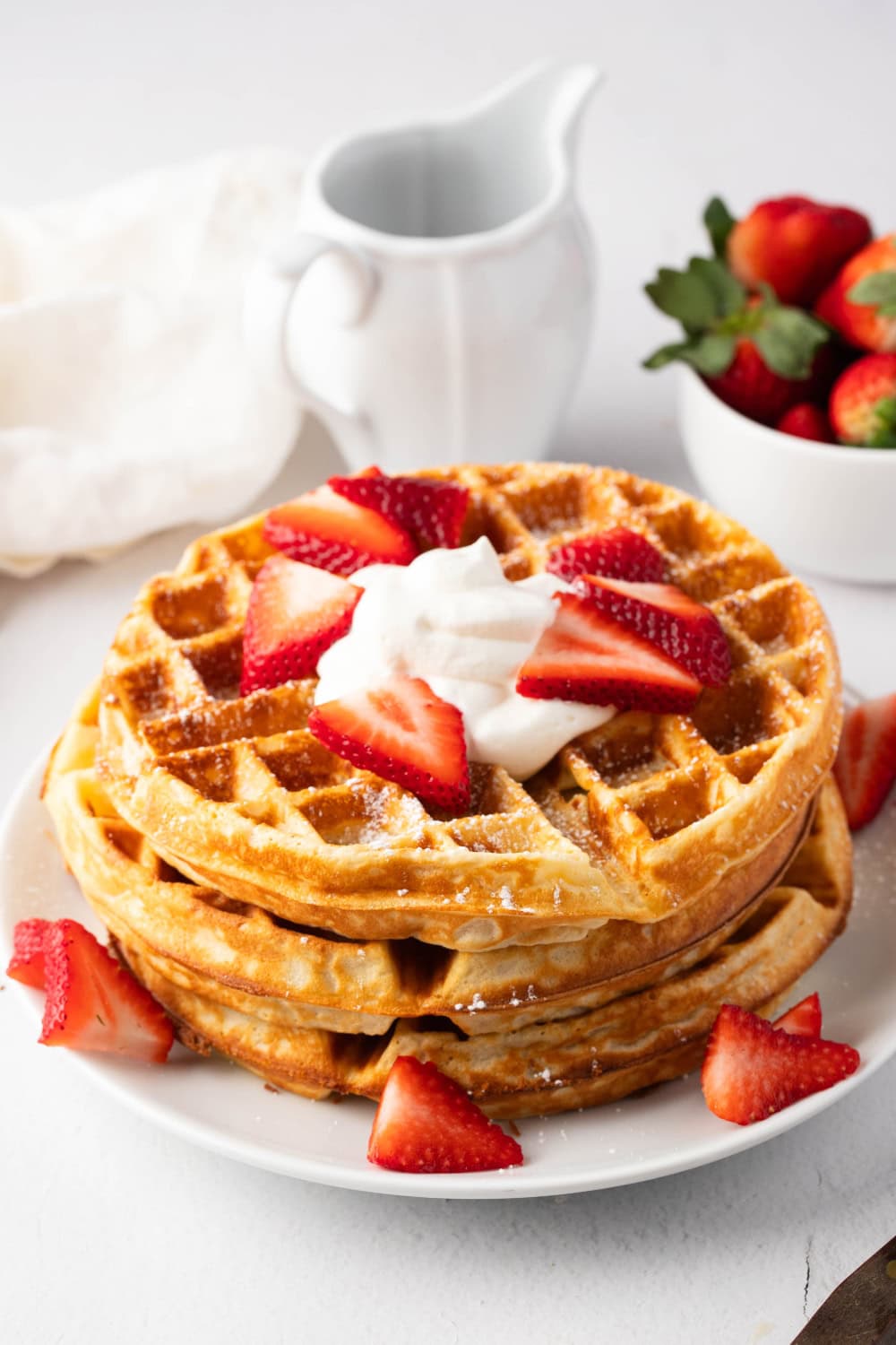 Stack of waffles with whipped cream and sliced strawberries on a white plate