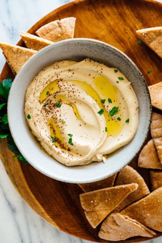 Hummus in a bowl with olive oil and feta bread on sides. 