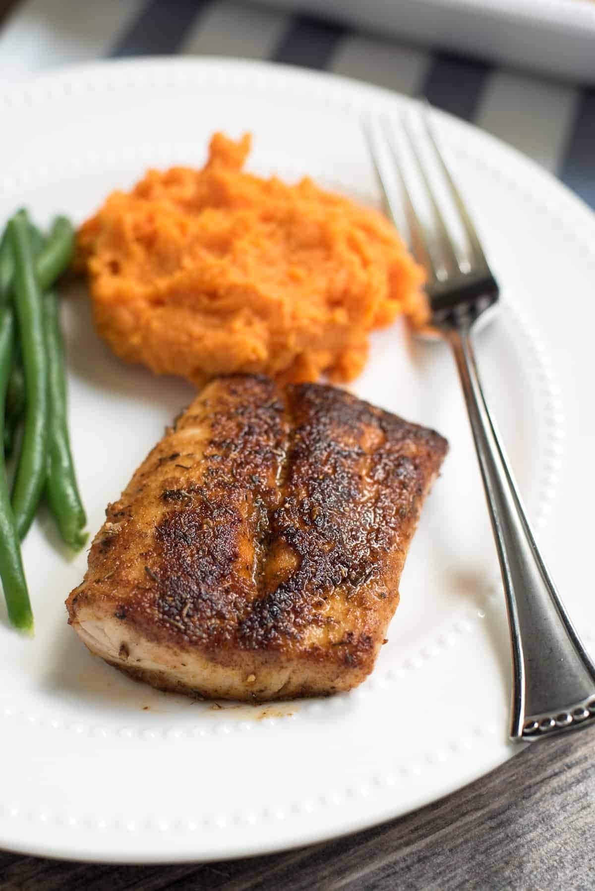 Grilled Mahi Mahi seasoned with Cajun mix  with green beans and sweet potato served on a plate with fork