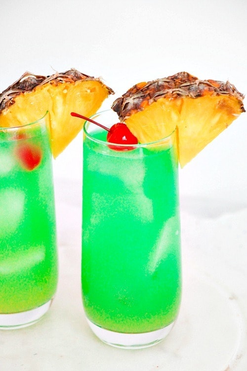 Two colorful glasses of pineapple-flavored drink served with slices of pineapple. 